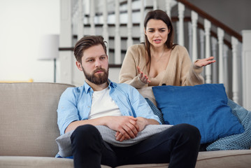 Confused man sits on the couch while his girlfriend yells and quarrels with him at home. Big family...