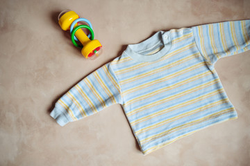 Tiny infant's shirt and kid's rattle on a beige background. Baby boy goods. Top view.