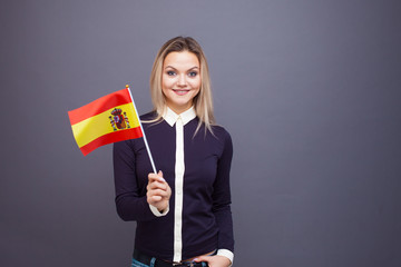 Immigration and the study of foreign languages, concept. A young smiling woman with a Spain flag in her hand.