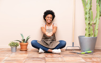 Gardener woman sitting on the floor holding copyspace imaginary on the palm to insert an ad