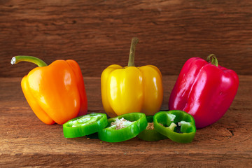 three large peppers paprika of different colors - red, yellow and orange, on a wooden background