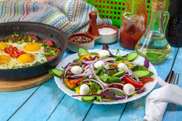 Fried eggs in a pan with cherry tomatoes and bell pepper for breakfast with salad