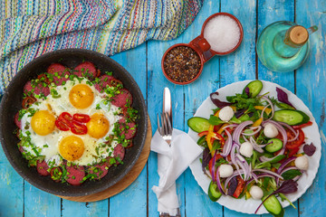 Fried eggs in a pan with cherry tomatoes and bell pepper for breakfast with salad