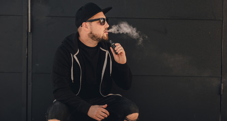 Young handsome man smoke with vape near black wall