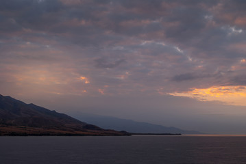 Fototapeta premium Lahaina, Maui, Hawaii, USA. - January 12 2012: Early morning light over ocean while approacing West side on dark ocean under spectacular cloudscape as if heaven is on fire. Shape of coastline hills.