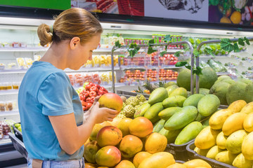 Young woman in a market, shop, choosing fresh ripe mango. Girl buying healthy exotic tropical raw...