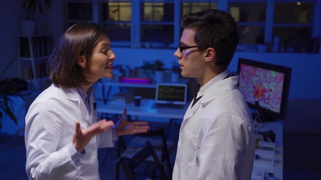 Side view medium shot of stressed male and female scientists in white coats arguing furiously standing face to face in biochemistry laboratory