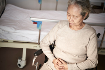 Obraz premium sad asian old woman sitting in wheelchair next to hospital bed