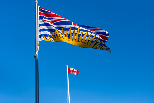 British Columbia flag flying with Canadian flag in background on a sunny day with blue sky  
