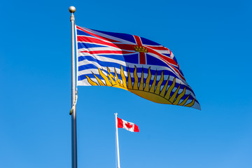 British Columbia flag flying with Canadian flag in background on a sunny day with blue sky  