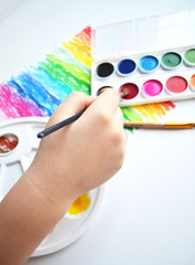 multicolored paints and brushes lie side by side on a white background. the child holds a brush in his hand