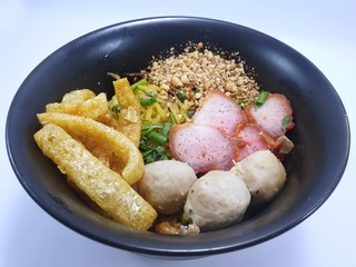 Top view of egg noodle topped with pork ball, roasted pork in black plate isolated on white background,  Ready to eat or serve