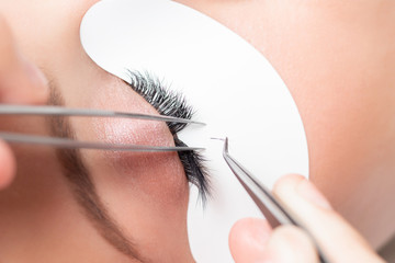 Naklejka premium Eyelash extension procedure. Master tweezers sets fake lashes on beautiful woman