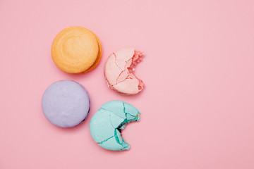 Bitten color macaroons on pink background, flat lay