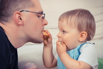 Preschooler with his father eating biscuit or cookies, dessert for kids and parental relations concept