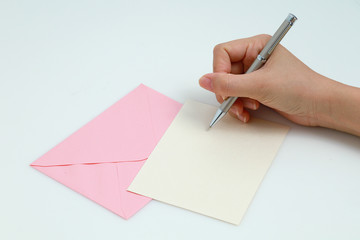 Woman's hands writing in blank note card with envelop. 