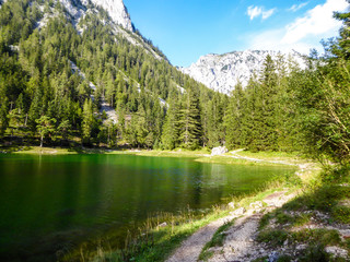 Fototapeta na wymiar A peaceful view on an Alpine valley in Austria. The valley has a Green Lake in the middle. Early spring in the mountains. There is a high mountain range in the back. Freshness. Few ducks on the lake.