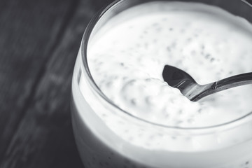 Plain yogurt with chia seeds in glass on the rustic wooden background. Selective focus. Black and white image.