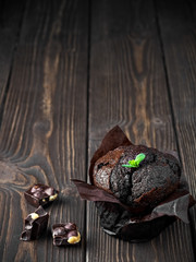 Homemade chocolate muffin with leaf mint on a wooden table. Near chocolate slices. Copy space, close up.