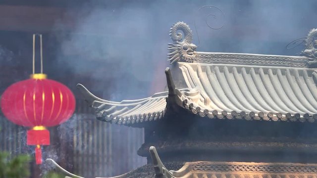 Smoke and ash raising up in the wind with traditional incense burner and temple building background, super slow motion, b roll shot.