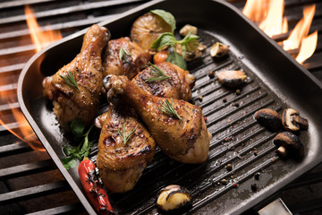 Grilled chicken leg with various vegetables on pan on the flaming grill