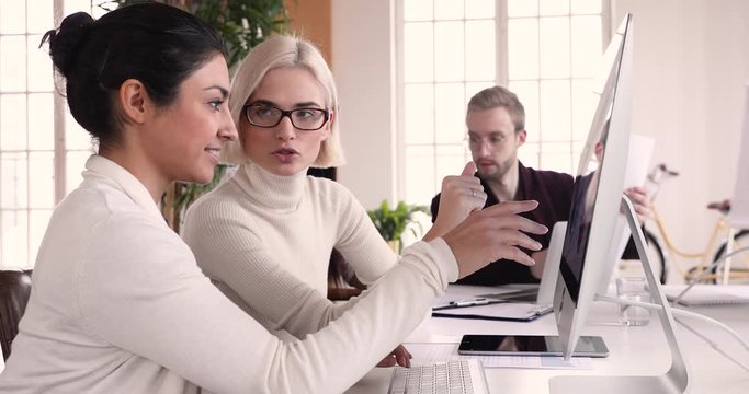 Diverse female coworkers discussing data working on computer at meeting