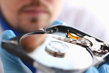 A male repairman wearing blue gloves is holding a hard drive from computer or laptop in hands....