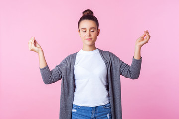 Yoga practice for mind balance. Portrait of calm brunette teenage girl with bun hairstyle in casual clothes standing with closed eyes. doing mudra gesture with fingers, meditation. indoor studio shot