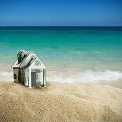 Naklejka premium house cut out of dollar bills on the sand. Concept on the topic of selling or buying a home.