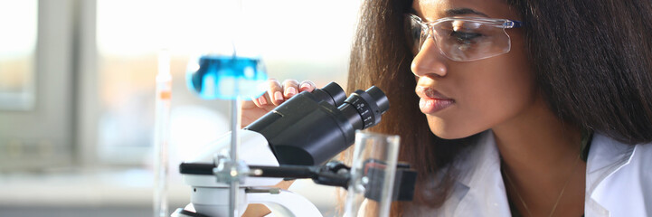Black woman scientist student chemist in protective goggles are conducting research using microscope for bacterial contamination of water to search for vaccine to treat diseases in medicine.