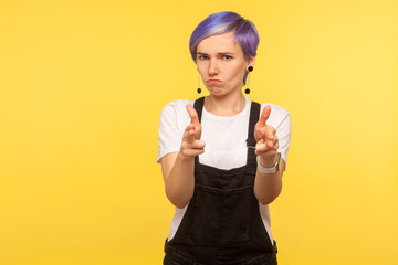 Portrait of dangerous hipster girl with violet short hair in denim overalls pointing handguns...