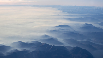 Fototapeta na wymiar Aerial view of the smog and fog that covers the Po Valley in Italy and the first mountains of the Alps. Landscape from airplane window. Pollution due to low rain and no wind
