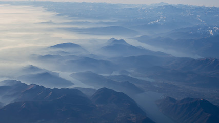 Naklejka na ściany i meble Aerial view of the smog and fog that covers the Po Valley in Italy and the first mountains of the Alps. Landscape from airplane window. Pollution due to low rain and no wind