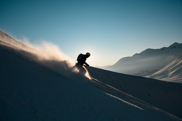 Silhouette of male skier rides down from the snowy hill top