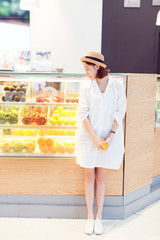 pretty woman holding an orange standing front of juice shop in shopping center.
