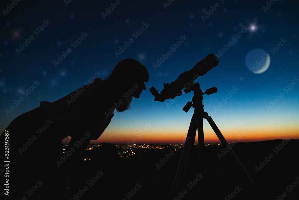 Wall mural astronomer with a telescope watching at the stars and moon with blurred city lights in the backgroun