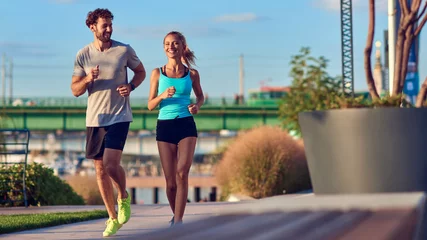 Poster Modern woman and man jogging / exercising in urban surroundings near the river. © astrosystem