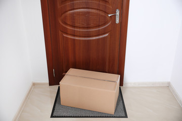 Cardboard box on rug near door. Parcel delivery service