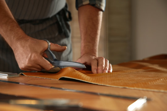 Man cutting leather with scissors in workshop, closeup