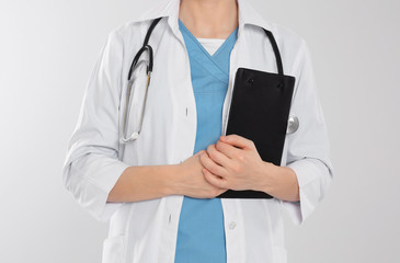 Doctor with stethoscope and clipboard on light grey background, closeup