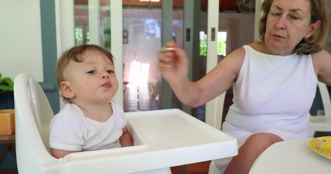 Grand-mother feeding adorable cute baby infant on highchair
