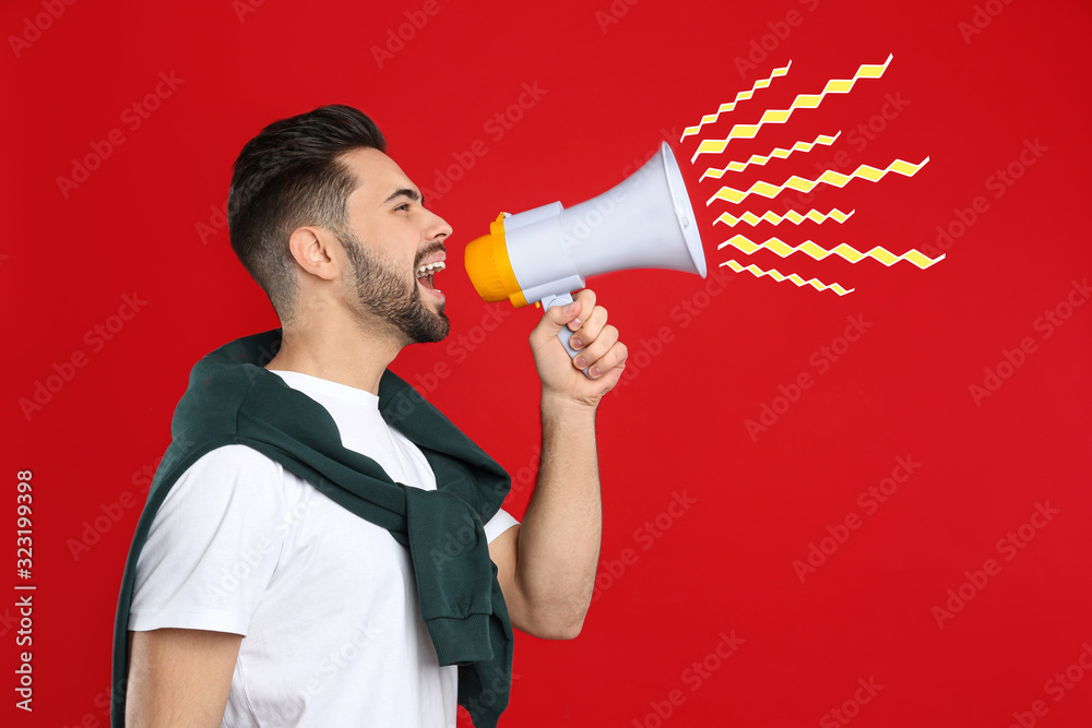 Wall mural Young man with megaphone on red background