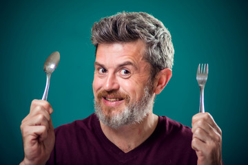 A portrait of bearded man holding spoon and fork in hands. People and food concept
