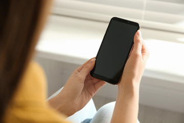 Young woman using modern smartphone indoors, closeup