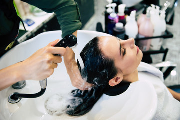 Warm water. Close-up photo of hairdresser&rsquo;s hands washing hair of young beautiful woman using shower.