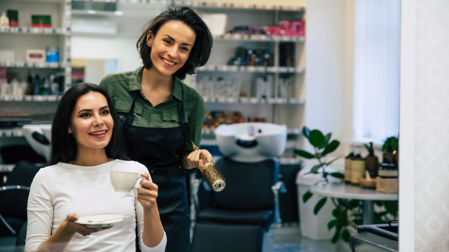 My favorite specialist. Close up photo of attractive woman with beautiful makeup drinking coffee and looking in the mirror while talking with a hairstylist.