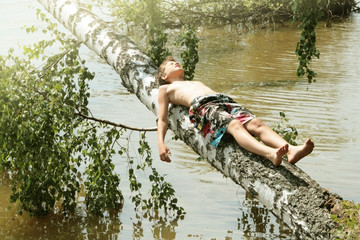 A 12-year-old tanned boy lies on a birch trunk that has fallen. Russian