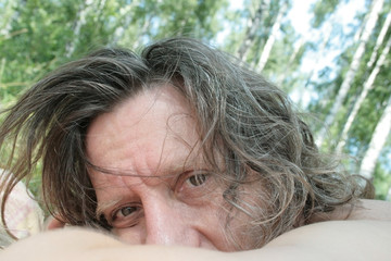 An elderly man with long hair in a birch grove looks carefully
