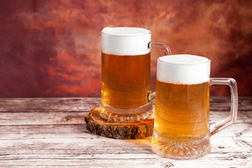 two beer mugs with foam on wood table