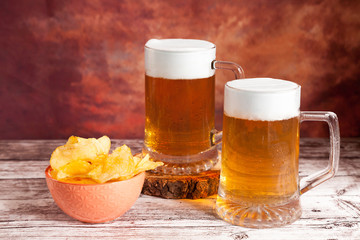two beer mugs with foam and bowl of chips